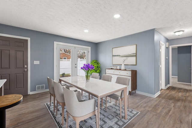 dining room with a textured ceiling, wooden walls, french doors, and dark hardwood / wood-style floors