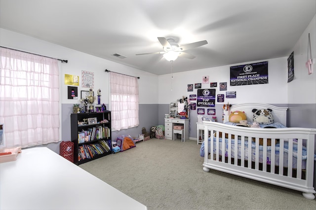 bedroom with carpet, ceiling fan, a nursery area, and multiple windows