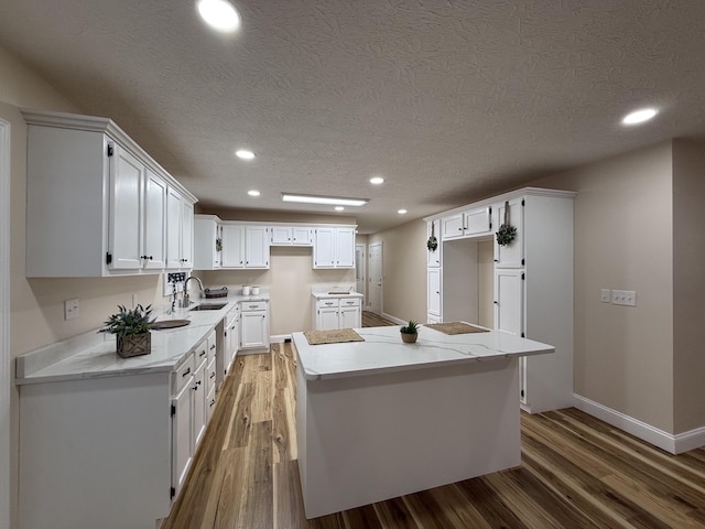 kitchen featuring hardwood / wood-style floors, a kitchen island, light stone counters, a textured ceiling, and white cabinets