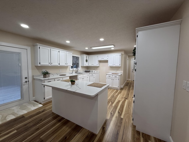 kitchen with a textured ceiling, wood-type flooring, a center island, and white cabinets