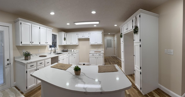 kitchen with white cabinetry, sink, a center island, light stone counters, and light wood-type flooring