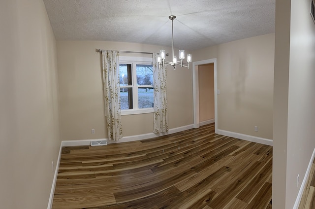 spare room featuring dark hardwood / wood-style floors, a chandelier, and a textured ceiling