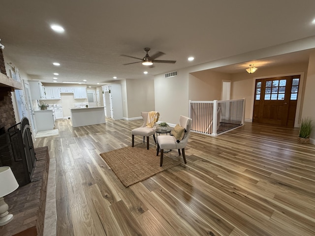 living room with ceiling fan, a brick fireplace, and light hardwood / wood-style flooring