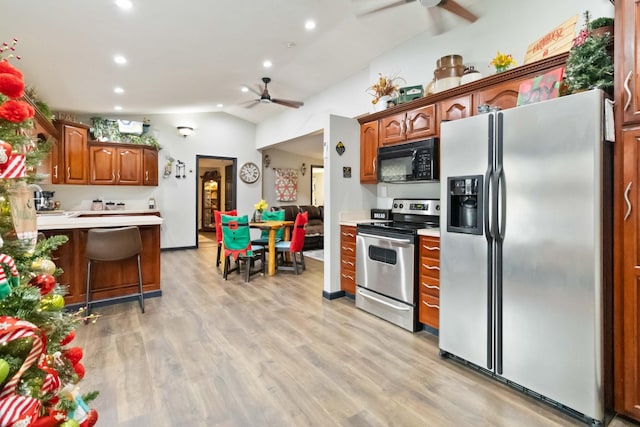 kitchen with vaulted ceiling, a breakfast bar area, appliances with stainless steel finishes, and light hardwood / wood-style flooring