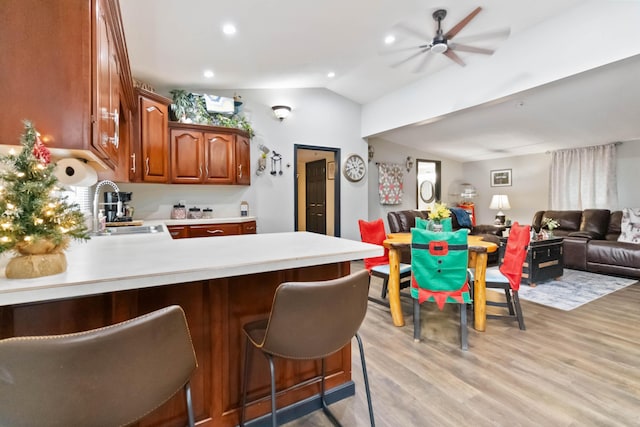 kitchen with lofted ceiling, sink, light hardwood / wood-style flooring, kitchen peninsula, and a breakfast bar area