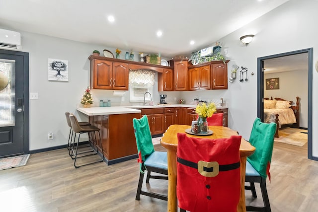 kitchen featuring a kitchen bar, kitchen peninsula, light wood-type flooring, a wall mounted AC, and sink