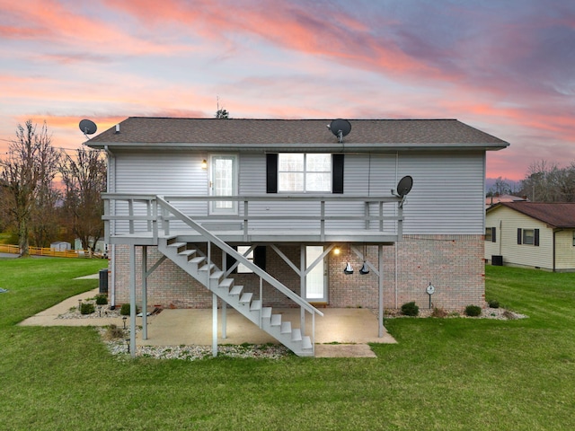 back house at dusk featuring a lawn, a deck, and a patio