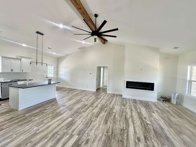 unfurnished living room with vaulted ceiling with beams, plenty of natural light, and light hardwood / wood-style flooring