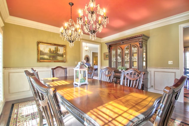 dining room featuring an inviting chandelier, wood finished floors, crown molding, and wainscoting