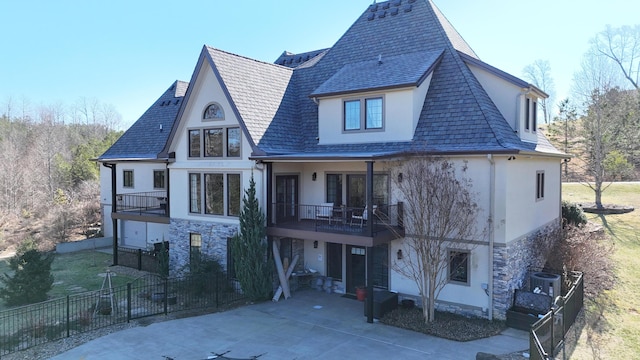 rear view of property with stucco siding, central AC, fence, a balcony, and stone siding