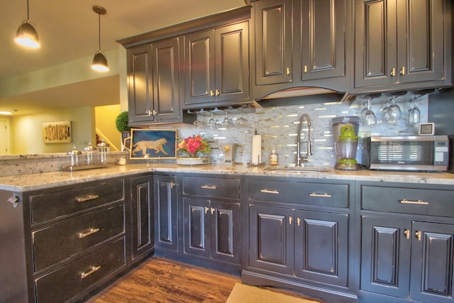 bar with decorative backsplash, stainless steel microwave, dark wood-type flooring, a sink, and indoor wet bar