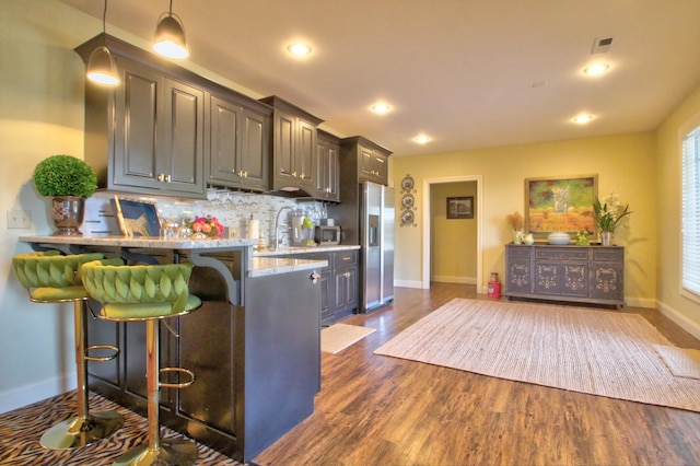 kitchen with a breakfast bar, dark wood-style flooring, visible vents, decorative backsplash, and stainless steel fridge with ice dispenser