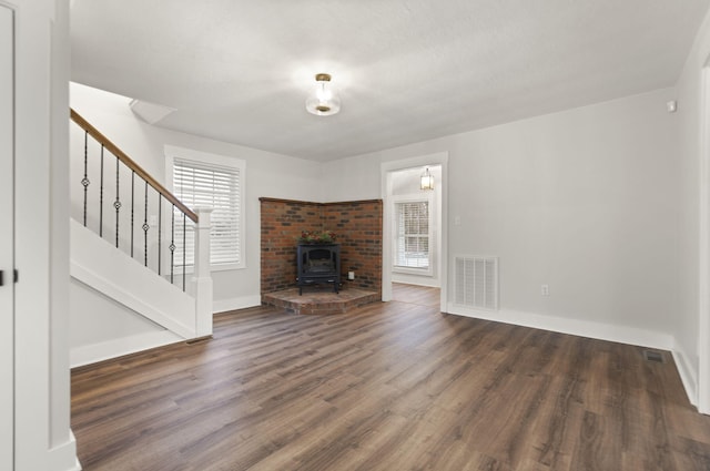 unfurnished living room featuring a wood stove, a wealth of natural light, and dark wood-type flooring