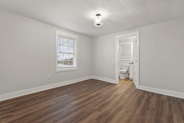 unfurnished bedroom featuring a textured ceiling, ensuite bathroom, and dark hardwood / wood-style floors