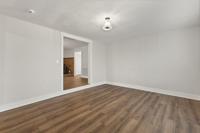 unfurnished room with dark hardwood / wood-style floors, a textured ceiling, and a brick fireplace