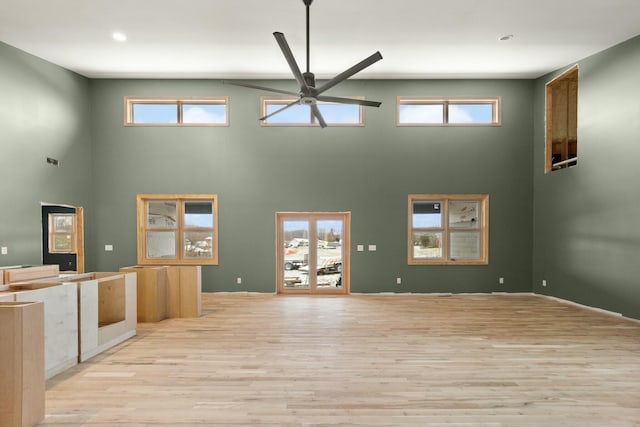 unfurnished living room with light wood-type flooring, ceiling fan, and a towering ceiling