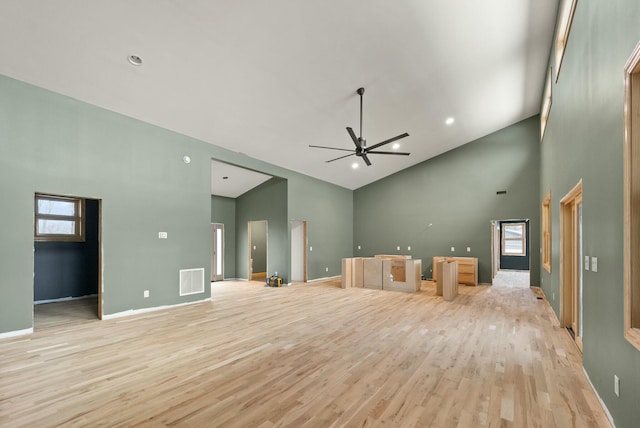 unfurnished living room featuring ceiling fan, a towering ceiling, and light hardwood / wood-style floors