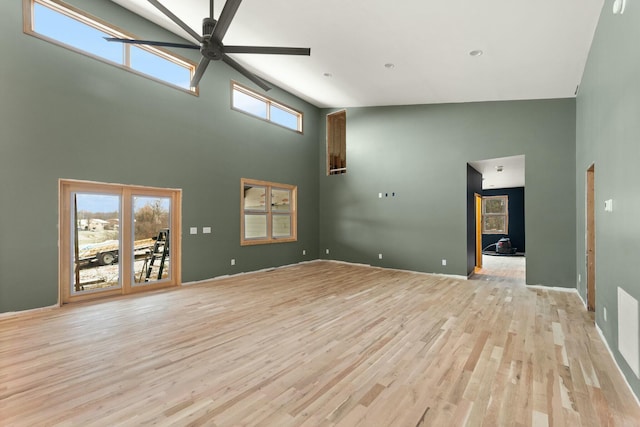 unfurnished living room with ceiling fan, light hardwood / wood-style floors, and a towering ceiling