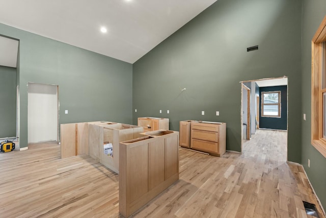 interior space featuring high vaulted ceiling, light hardwood / wood-style floors, and light brown cabinetry