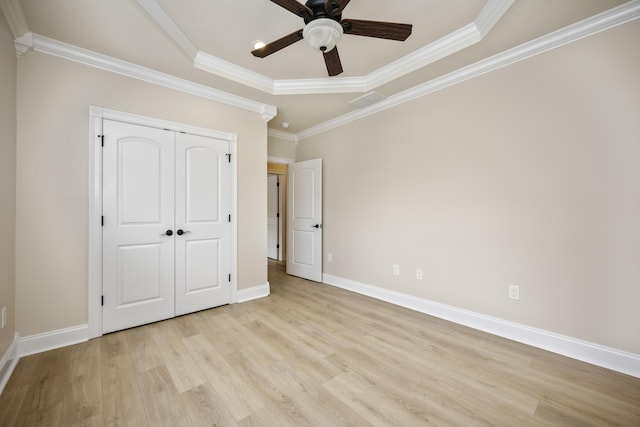 unfurnished bedroom with a raised ceiling, light hardwood / wood-style flooring, ceiling fan, ornamental molding, and a closet