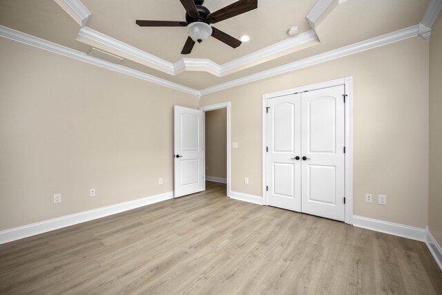 unfurnished bedroom featuring ceiling fan, crown molding, light hardwood / wood-style floors, a tray ceiling, and a closet