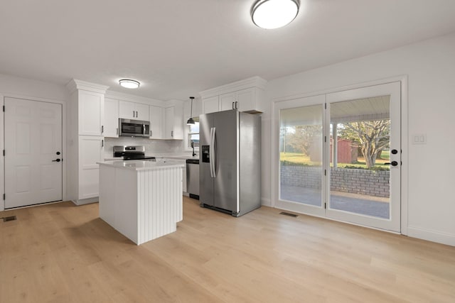 kitchen with light wood-type flooring, stainless steel appliances, decorative light fixtures, a center island, and white cabinetry