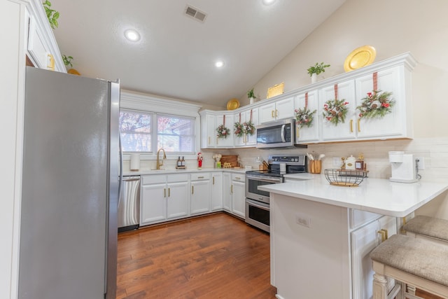 kitchen with white cabinetry, dark hardwood / wood-style floors, kitchen peninsula, a kitchen bar, and appliances with stainless steel finishes