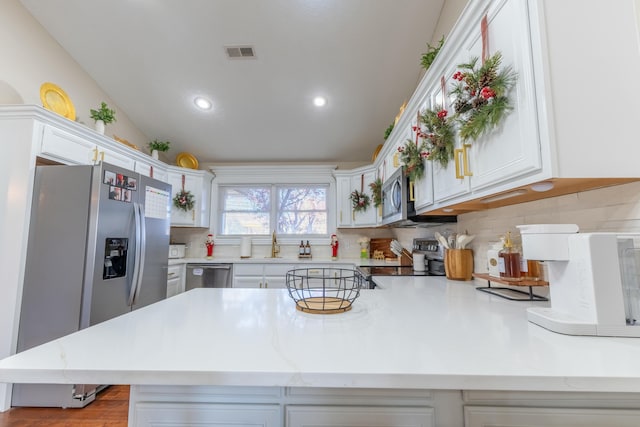 kitchen featuring kitchen peninsula, appliances with stainless steel finishes, backsplash, vaulted ceiling, and white cabinetry