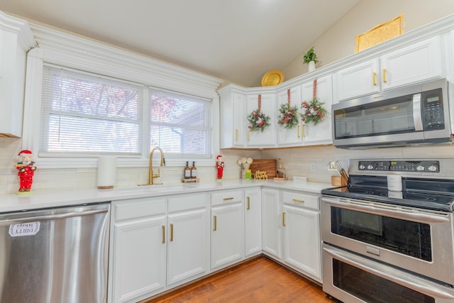 kitchen with appliances with stainless steel finishes, vaulted ceiling, white cabinetry, and sink