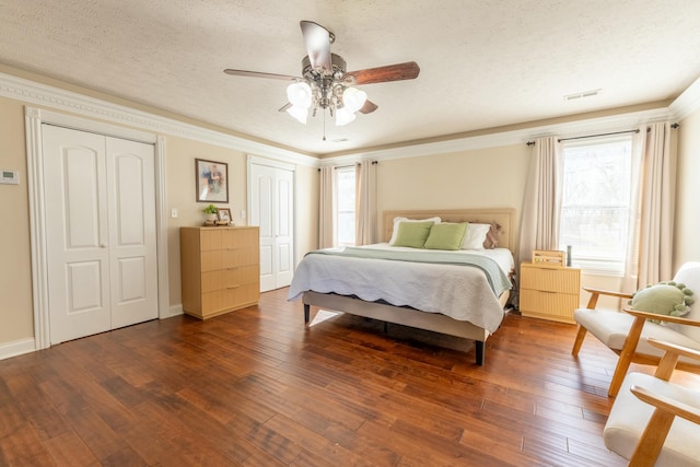 bedroom with ceiling fan, dark hardwood / wood-style floors, a textured ceiling, and two closets