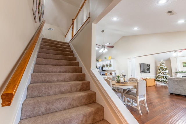 staircase with ceiling fan, wood-type flooring, and lofted ceiling