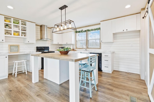 kitchen featuring white cabinetry, wall chimney exhaust hood, a center island, and black appliances