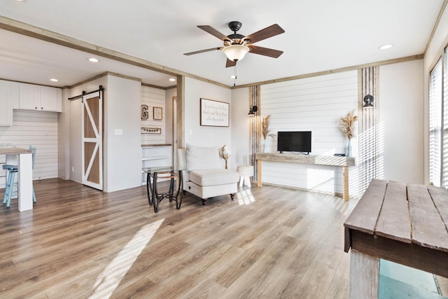 living room featuring ceiling fan, a barn door, light hardwood / wood-style floors, and wood walls