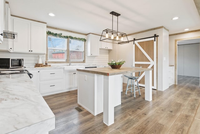 kitchen with decorative light fixtures, white cabinets, a center island, a barn door, and light hardwood / wood-style flooring