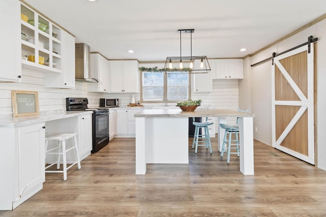 kitchen with a kitchen bar, a barn door, black electric range, and wall chimney range hood