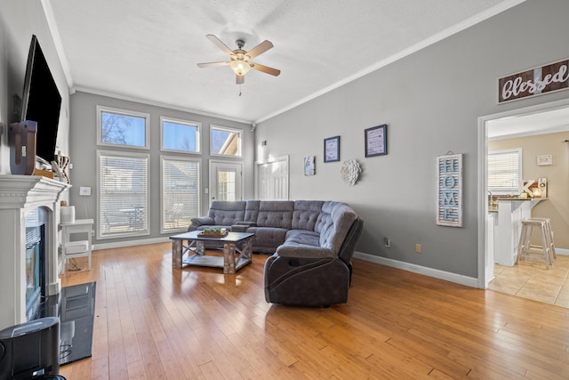 living room featuring crown molding, ceiling fan, light wood-type flooring, a textured ceiling, and a tiled fireplace