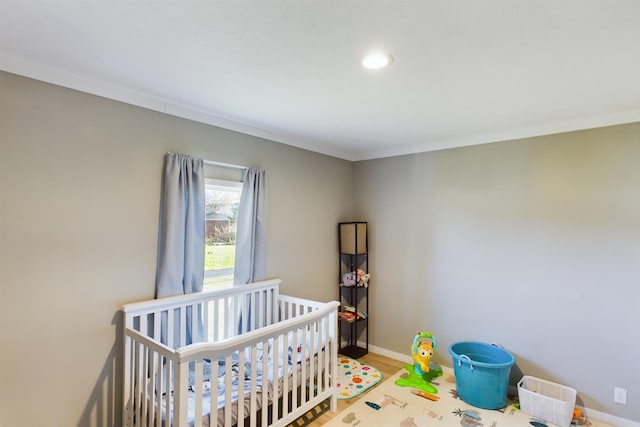 bedroom with light hardwood / wood-style floors, a crib, and ornamental molding