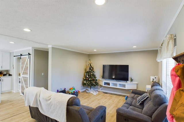 living room with a barn door, ornamental molding, and light wood-type flooring