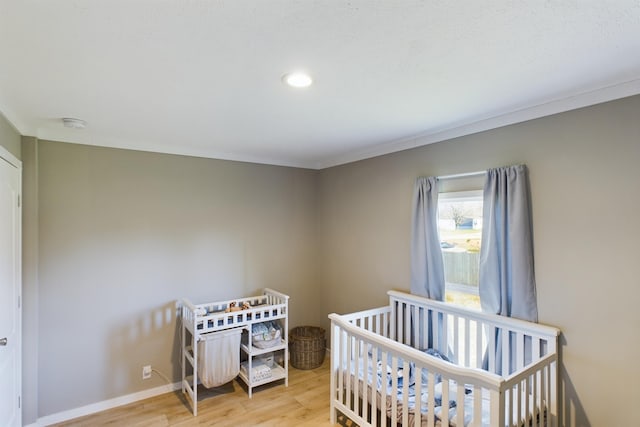 bedroom featuring a nursery area, ornamental molding, and light hardwood / wood-style flooring