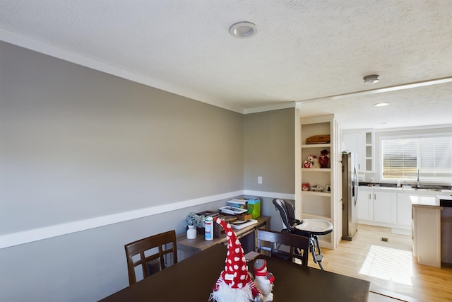 dining space with light wood-type flooring, a textured ceiling, and ornamental molding