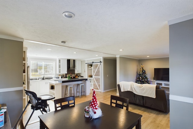 dining area featuring sink, a barn door, ornamental molding, a textured ceiling, and light hardwood / wood-style floors