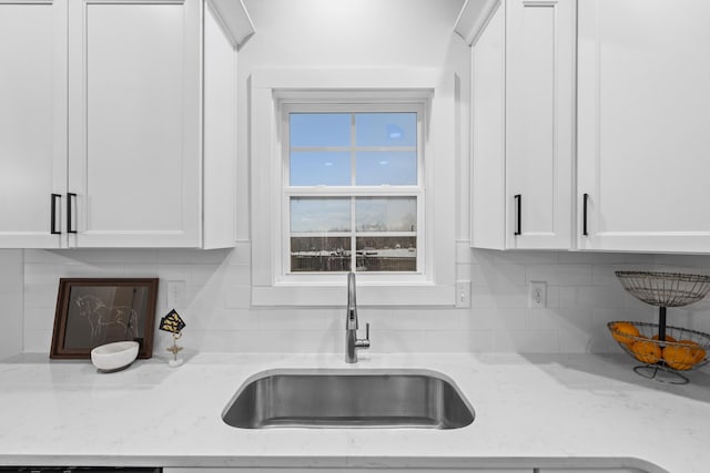 kitchen with white cabinets, backsplash, light stone counters, and sink