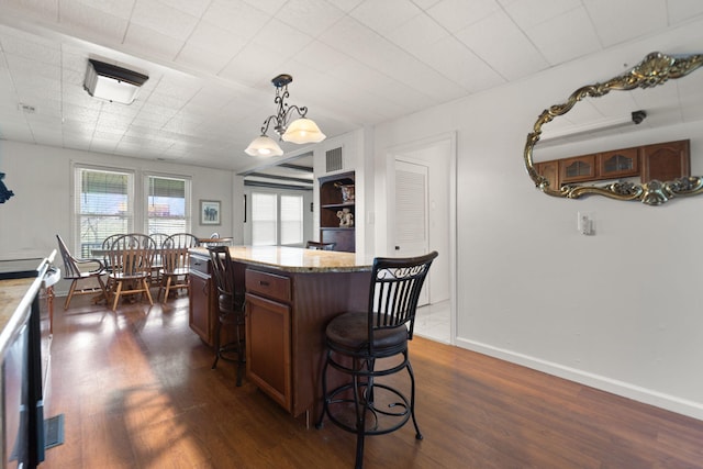 kitchen with dark hardwood / wood-style flooring, decorative light fixtures, a kitchen island, and light stone counters