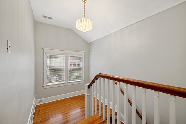 stairway with an inviting chandelier, hardwood / wood-style flooring, and vaulted ceiling