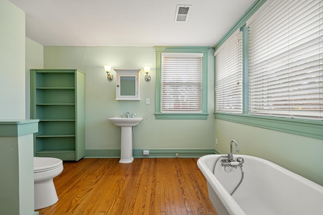 bathroom with hardwood / wood-style floors, a washtub, and toilet