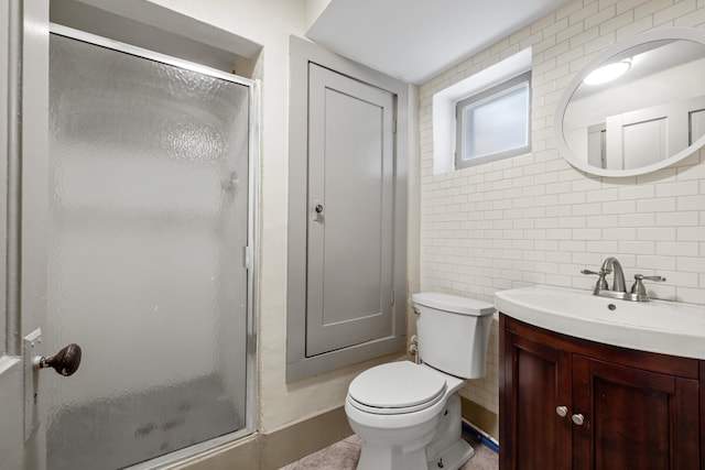 bathroom with vanity, toilet, a shower with shower door, and tile walls