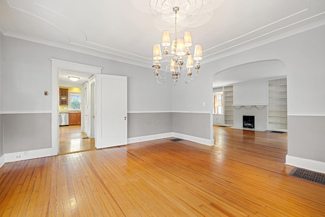 interior space featuring ornamental molding, light hardwood / wood-style floors, a brick fireplace, built in shelves, and a chandelier