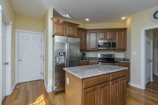 kitchen with light stone countertops, appliances with stainless steel finishes, a center island, and light hardwood / wood-style flooring