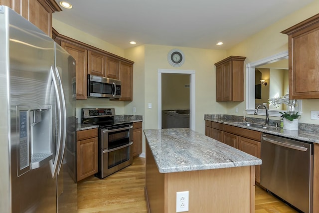 kitchen featuring a center island, sink, light hardwood / wood-style flooring, light stone countertops, and stainless steel appliances