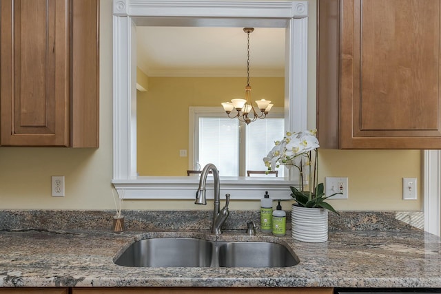 kitchen featuring pendant lighting, dark stone counters, an inviting chandelier, sink, and ornamental molding